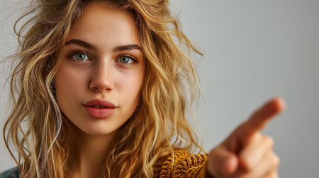 Portrait of a young beautiful Caucasian blonde woman on a gray background pointing her finger at camera.の素材