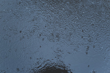 Top view dark water surface with raindrops, rain shower outdoors.