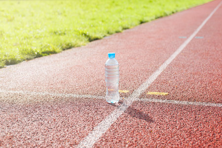 Plastic bottle of water in the stadium on the treadmill, outside. Sunny clear day. Healthy...
