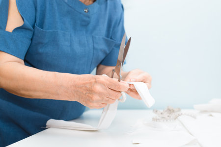 Dressmaker at work at home. Close-up of an elderly seamstress's female hands holding cloth and...