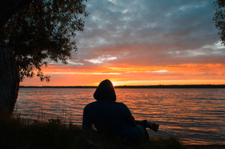 Man relaxing by the lake at sunset. Silhouette of person lying and looking at the setting sun....