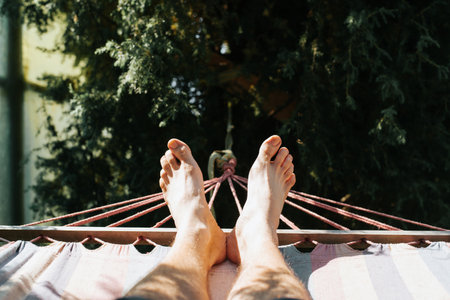 Barefoot man lying resting in hammock outdoors on sunny summer day. Selective focus on caucasian...
