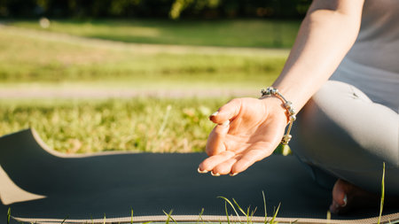Meditation and yoga in the morning outdoors. Close-up of a woman sitting in a lotus position on a yoga mat and meditating at sunrise, selective focus on a woman's hand. Copy space. Cropped image.の写真素材