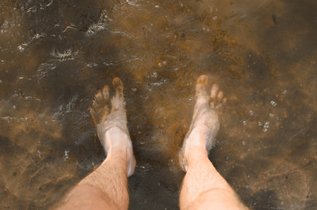 Top view of a man standing barefoot in muddy water, close-up of male bare feet in sand and mud....