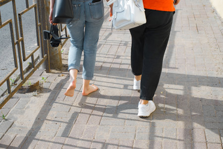 Girlfriend walking barefoot on sidewalk holding high-heeled shoes, back view. Close-up of bare feet...