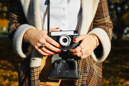 Close-up young hipster woman holding retro film camera, taking photo outdoors. Girl photographer and vintage camera, hobby and lifestyle. Selective focus on old technique and female hands.の写真素材