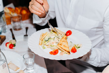 Man eating tomato salad, crackers, greens from a plate indoors, close-up. Festive feast concept. selective focus on food.の写真素材