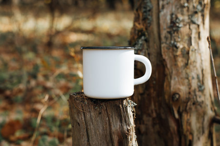 Empty enamelled camping mug mock up standing on tree stump in woods outdoors. Blank new metal cup for logo or branding, close-up.の写真素材