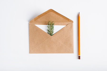 Christmas, Happy New Year minimal composition, flat lay. Top view open craft envelope, white card, pine twig and pencil on white table. Holiday message concept, greeting card.の写真素材