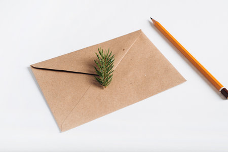 Christmas closed craft envelope with twig of pine and pencil lying on white table. Concept for festive invitation, xmas wish, Happy New Year or Merry Christmas greetings.の写真素材