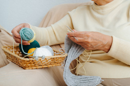 Knitting hobby, needlework, handcraft, active leisure retirement concept. Close-up of senior woman holding threads and needles, knitting scarf while sitting on sofa at home. Cropped image.の写真素材