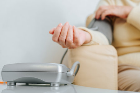 Close-up of senior sick woman checking her blood pressure and pulse indoors. Selective focus on tanometer, medical measuring instrument. Hypertension, elderly and healthcare.の写真素材