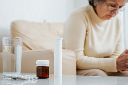 Seniors and health care, treatment, medication concept. Lonely elderly sad woman sitting on an armchair next to bottle of pills, indoors. Selective focus on medicine bottle, close-up.の写真素材