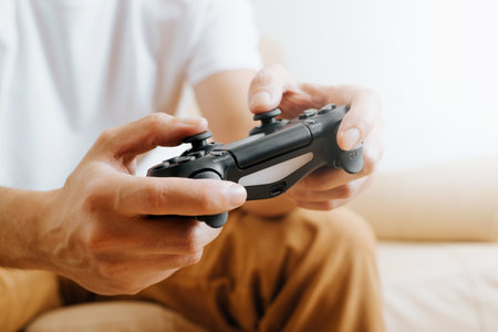 Close-up of man pushing buttons of wireless device of gamepad while sitting on sofa at home, side...
