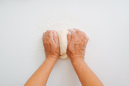 Top view senior woman cook kneads dough on white table in home kitchen. Female wrinkled hands in flour, making bread or homemade baking. Pov.の写真素材