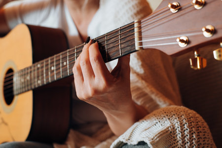 Musical hobby, learn music concept. Close-up of woman playing an acoustic guitar, indoors. Selective...