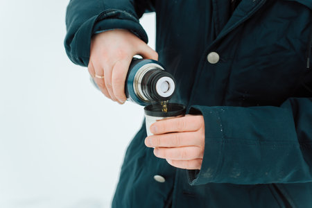 Hike, travel, tourism, warm drink in cold weather concept. Close-up of man in winter jacket pours...
