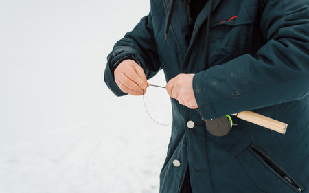 Close-up of man fisherman holding fishing rod, pulling line for winter fishing, outdoors.