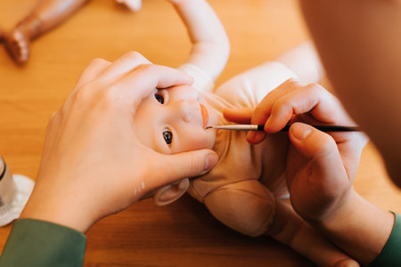 Reborning, puppet craft, hobby concept. Young female craftsman decorating realistic newborn doll...