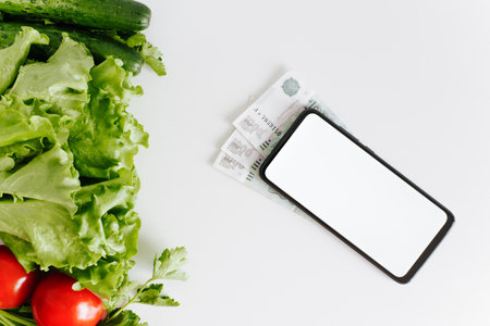 Eco vegetables, money and mobile phone mockup on white table top view. Smartphone with white empty...