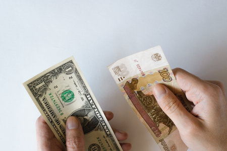 Human hands holding one US dollar and one hundred rubles on white background top view, close-up....