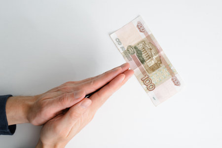 Unrecognizable person prays for money. Close-up of human caucasian palms folded in prayer for one hundred rubles on white background, top view. Concept poverty, poor, hope.の写真素材