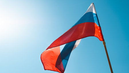 National flag tricolor of Russian Federation waving in wind against clear blue sky on sunny day,...