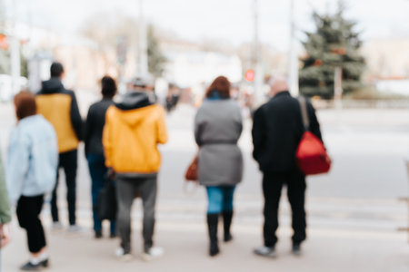 Back view of crowd of pedestrians standing at crossroads waiting for traffic signal outdoors, out of...
