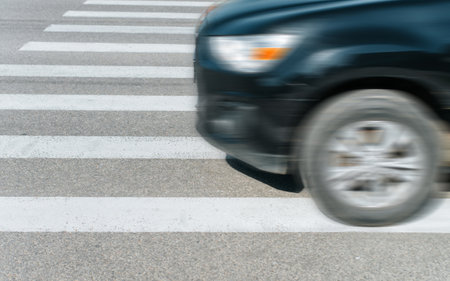 Black blurred car driving fast on crosswalk, outdoors.. Close-up, side view, selective focus on white markings of pedestrian crossing.の写真素材