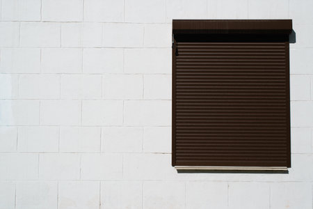 Window closed with roller shutters exterior view of white wall of building outdoors, copy space.の写真素材