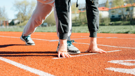 Outdoor workout. Close-up of woman practicing running on stadium treadmill, standing at low start on sunny day, frontal view. Sports, active lifestyle.の写真素材