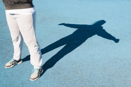 Woman exercising outdoors, sportswoman lifting up dumbbells on sports ground on sunny day. Selective focus on shadows, close-up.の写真素材