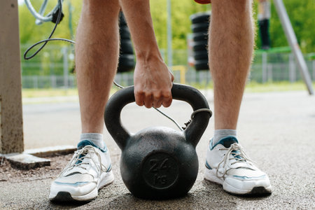 Weightlifting workout outdoors. Close-up of man holding heavy kettlebell while standing on sports...