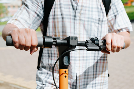 Man using electric scooter outdoors on sunny day. Close-up of male caucasian hands holding steering wheel rented scooter, selective focus.の写真素材