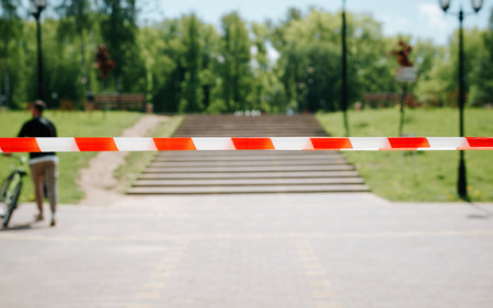 Closed area for quarantine. Protective signal tape at entrance to park, outdoors. Selective focus on striped red white ribbon.の写真素材