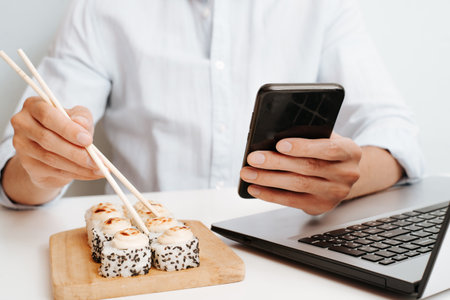 Businessman using mobile phone during lunch while sitting at table with laptop indoors. Close-up...