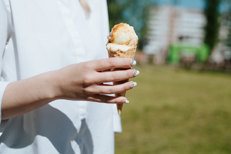 Side view of woman's hand holding an ice cream waffle cone on sunny day outdoors, close-up....