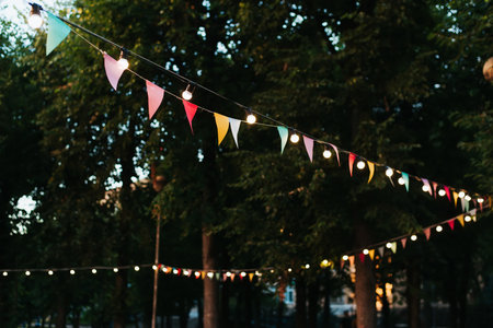 Multicolored decorative festival flags and light bulbs garland on street on summer evening. Selective focus.の写真素材