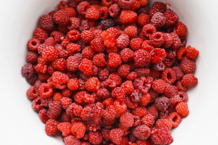 Top view red ripe raspberries picked from garden in white bowl, close-up.