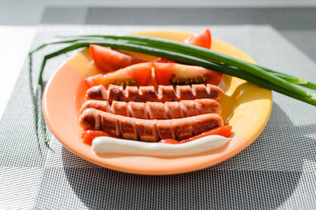 Close-up of fried sausages, tomatoes, green onions with ketchup and mayonnaise on plate inside. Selective focus on sausageの写真素材