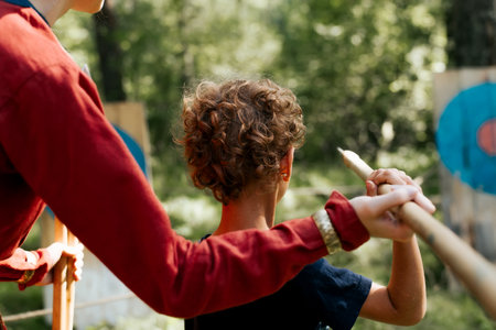 Back view of little curly boy learning to throw a javelin at a wooden target, outdoors. Festival of...