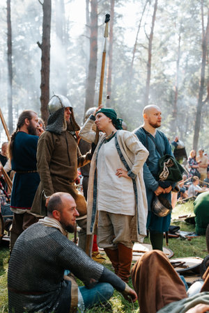 Vikings in a helmet with a spear and a woman in an ancient costume in the forest at a halt in the forest. Medieval Reconstruction Festival. Smolensk, Russia 08/13/2022.の写真素材