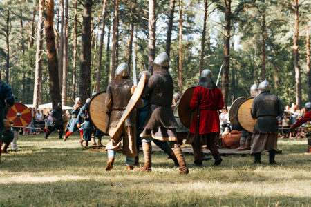 Knights and Vikings with swords, shields and helmets fighting in the forest at the festival of historical reenactment. Smolensk, Russia 08/13/2022.の写真素材
