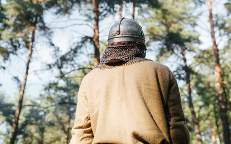 Back view of a lone medieval warrior in a steel helmet standing in a forest outdoors.の写真素材