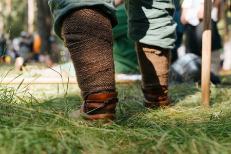 Close-up of a Viking leg in protective braid. Warrior standing on grass outdoors, low angle view.の写真素材