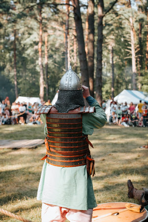 Viking warrior in armor puts on a helmet as he prepares for battle at a festival of historical...