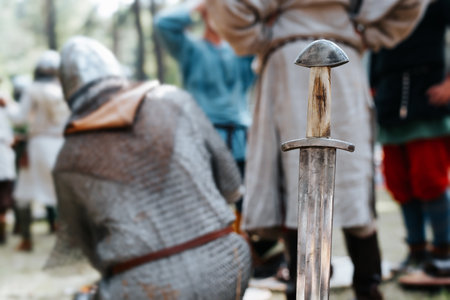 Medieval old steel sword against the background of knights outdoors. Close-up, selective focus on...