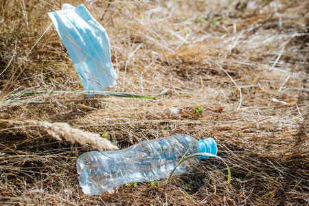 Used plastic bottle and medical face mask on dry grass, top view. Garbage in nature, environment pollution concept.の写真素材