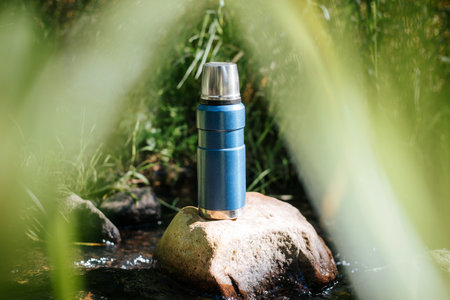 Thermos outdoors. Vacuum camping flask standing on a stone in the water.の写真素材