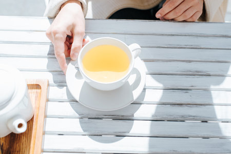 Close-up of female hands holding mug of tea in street cafe, top view.の写真素材